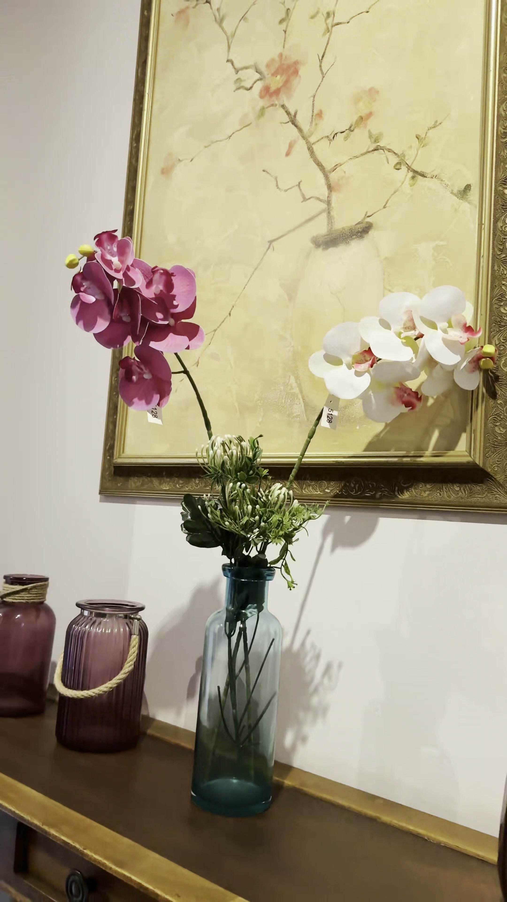 Orquídeas y flores frente a un cuadro con marco dorado