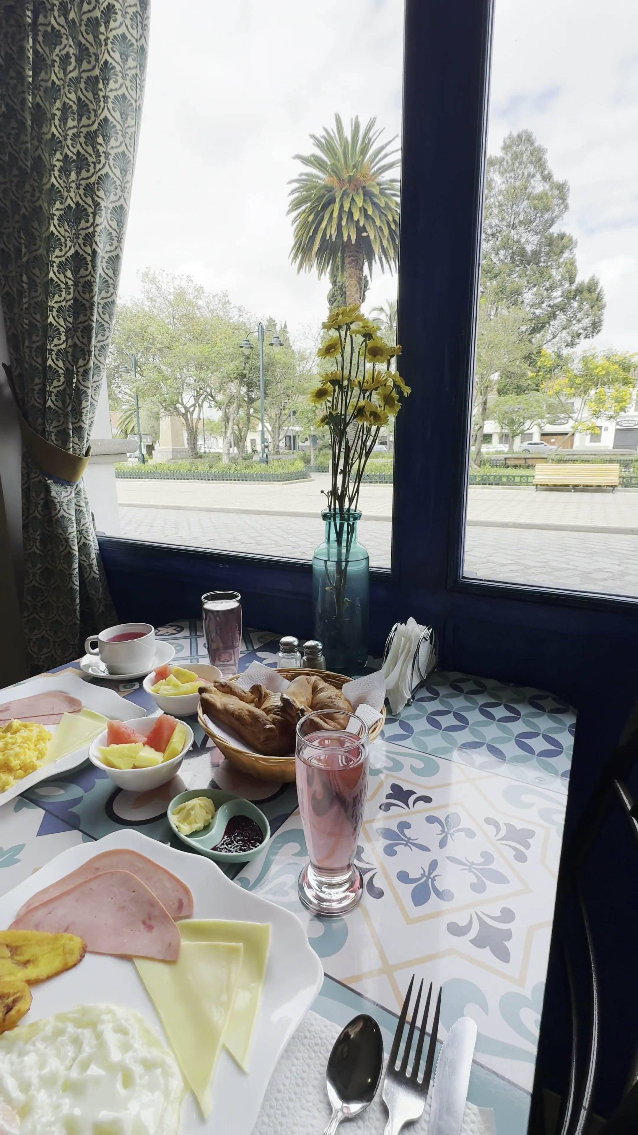 Mesa de desayuno con frutas, embutidos, quesos y jugo junto a la ventana