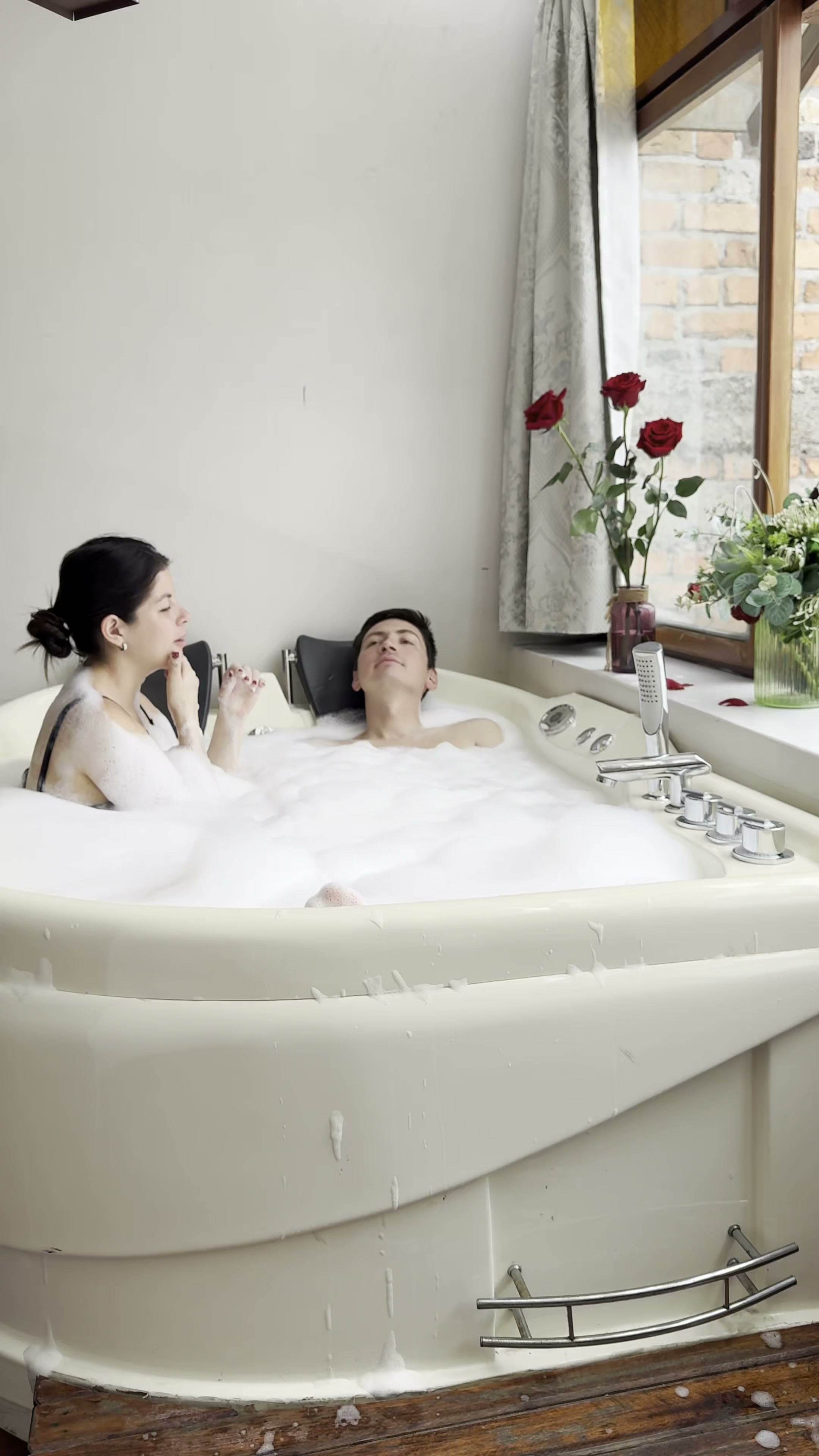 Pareja disfrutando del jacuzzi de la habitación junto a la ventana