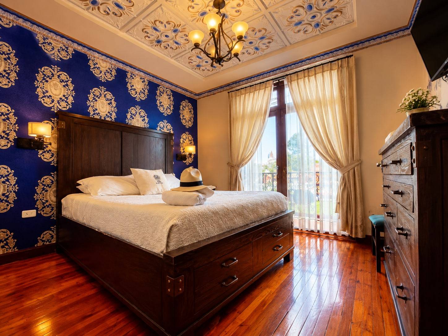 Habitación matrimonial con pared azul ornamentada, cama de madera y puerta al balcón