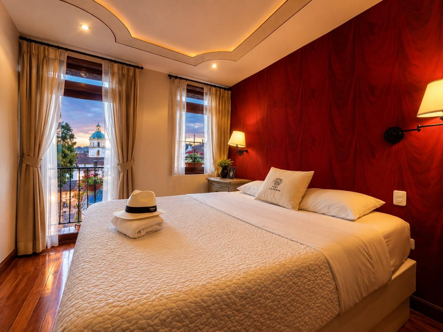 Cama matrimonial junto a la puerta del balcón con vista a la ciudad al atardecer
