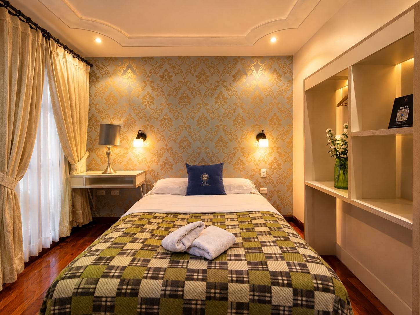 Habitación matrimonial interna con papel tapiz dorado, lámparas de pared y repisas
